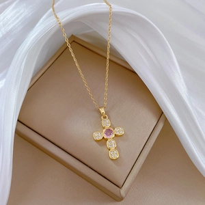 Detail of gold cross necklace with pink gemstone and white crystals on a jewelry box