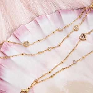 Detailed close-up of golden double-layer beaded bracelet with heart and diamond charms