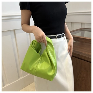 Detail view of a bright green pleated leather handbag with a minimalist single handle design