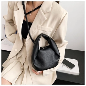 Detail of a black pebbled leather pleated cloud bag worn with a beige blazer