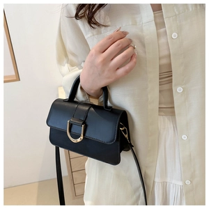 Minimalist black handbag with gold horseshoe buckle worn by model as a stylish shoulder bag