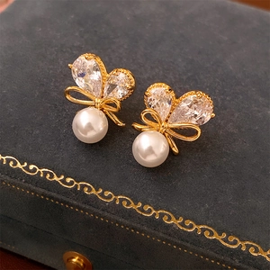 Vue macro des boucles d'oreilles nœud doré avec perle blanche et zircon sur un écrin bleu