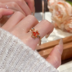 Detailed close-up of 18k gold maple leaf ring with orange zircon on model hand