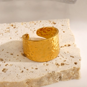 Golden hammer textured wide open ring in stainless steel displayed on a stone pedestal