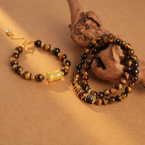 Detail of tiger eye bead bracelets with golden charms on a textured brown background