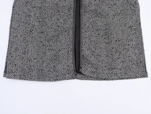 Detail of herringbone tweed texture with black faux leather trim on a loose winter coat