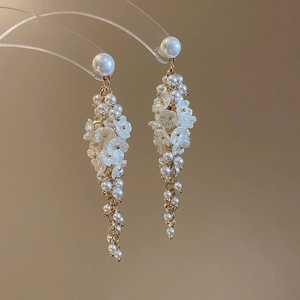 Detail of elegant pearl flower earrings with long gold chain tassels hanging on display