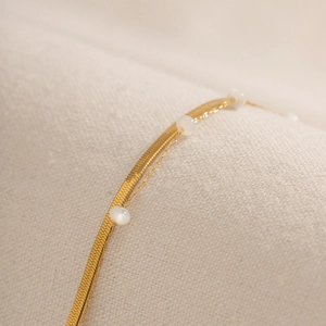 Detail of 18K gold snake chain necklace with white beads on soft textured fabric