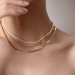 Detailed layered look of white pearl choker and 14K gold plated snake chain on model neck