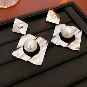 Macro detail of geometric silver earrings with large round pearls and diamond accents