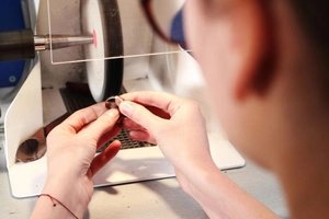 Close-up of craftsman hands polishing a minimalist stainless steel ring on a workbench
