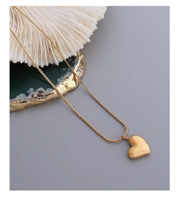 Detail of 18k gold plated heart pendant necklace with twisted rope chain on coral