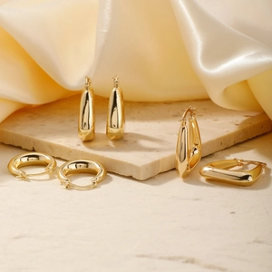Three gold earrings in hoop and drop styles on white marble with beige silk fabric
