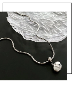 Close-up of a polished silver box chain necklace with a pebble-shaped pendant