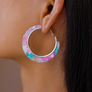 Macro shot of large pink and blue marble pattern resin hoop earrings on model