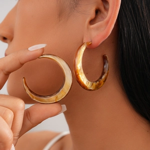 Close-up of large C-shaped resin hoop earrings with brown marble tortoise shell pattern