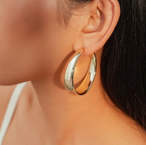 Close-up of a wide polished gold C-shaped hoop earring worn by a model for a chic look