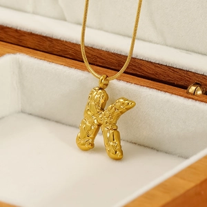 Macro detail of gold letter K pendant with unique rock texture on a sleek snake chain