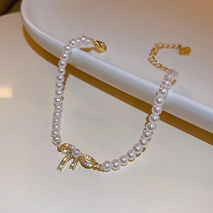 Detail of gold bow charm with white pearls and adjustable heart tail chain closure