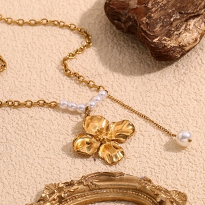Close-up of 18K gold-plated flower pendant and white pearls on a textured background