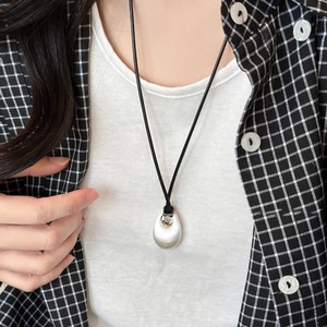 Oval silver pendant necklace with black cord shown on a model with a plaid shirt