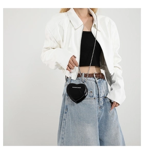 Detail of glossy black heart-shaped crossbody bag with silver chain and white lettering