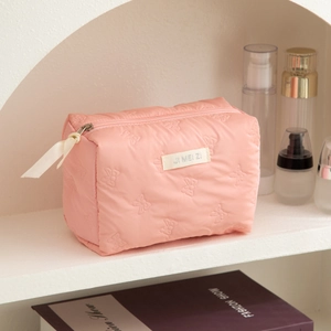 Detail of pink quilted makeup bag with bow texture and cream ribbon zipper pull