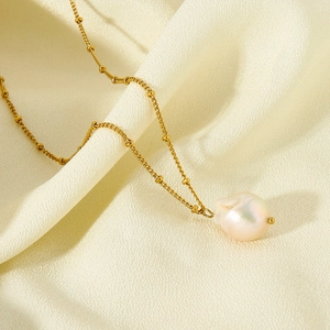 Golden fine chain necklace featuring a natural baroque pearl pendant on silk background