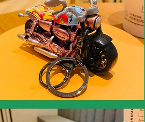 Detail of metal motorcycle keychain featuring purple finish and vintage street art patterns