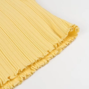 Gros plan détaillé du haut en tricot jaune avec texture côtelée et poignets volantés