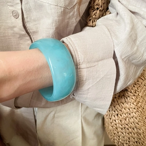 Detail of wide sky blue resin bangle showing smooth polished finish on a female wrist