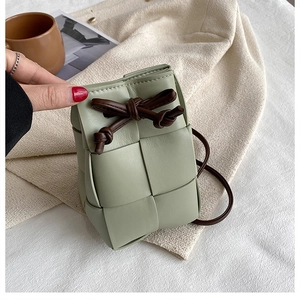 Close-up of hand-woven light green bucket bag with brown leather drawstring closure