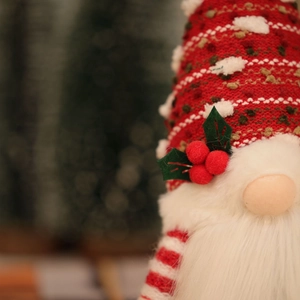 Close-up of a knitted Christmas gnome with glowing nose and red berry hat details