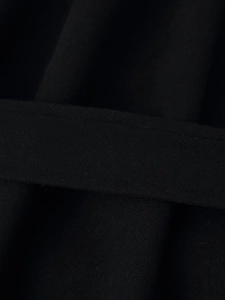 Gros plan sur la texture en laine noire et les coutures plates de ce manteau chic
