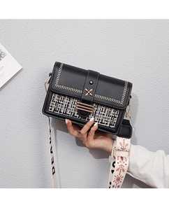 Close-up of black leather crossbody bag featuring gold floral buckle and tweed texture