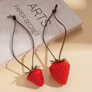 Unique leather cord necklace with red resin strawberry pendants on a neutral book