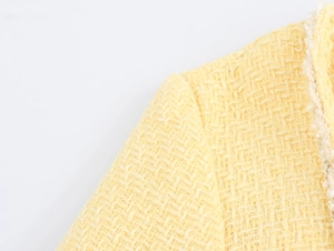 Detail of the yellow tweed fabric texture and woven trim on the shoulder of a mini dress