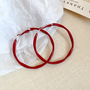 Detail of red oversized twisted hoop earrings with glossy finish on textured background