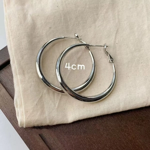 Detail shot of 4cm silver hoop earrings on a textured base showing size and metal finish