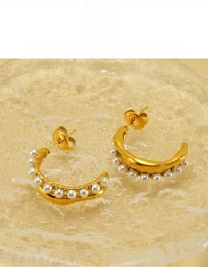 Detailed close-up of golden C-shaped earrings with white pearls and butterfly backings