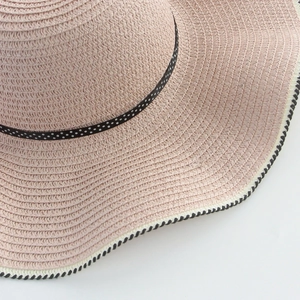 Detail of pink straw sun hat with black polka dot ribbon and wavy border edge