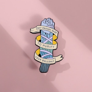 Creative enamel pin with sage bouquet and motivational text ribbon on pink background