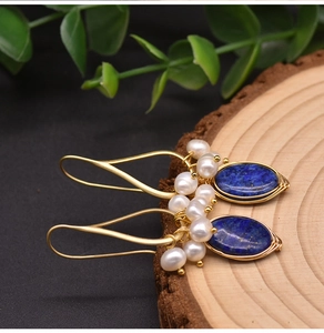Detail of wire-wrapped natural pearl and blue lapis lazuli earrings on wooden slice