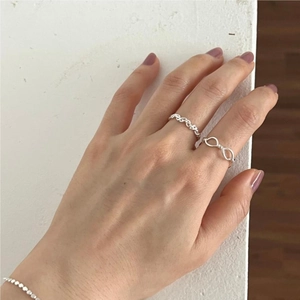Hand wearing silver twisted rope ring and infinity link ring set on a white surface
