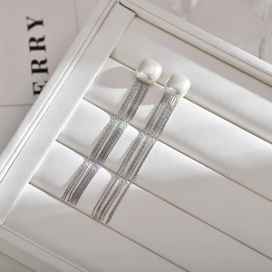 Macro detail of long silver tassel earrings with white square pearls in a jewelry box