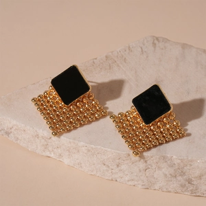 Detail shot of woven gold mesh diamond earrings with black enamel on a stone surface