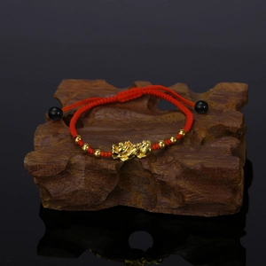 Detail of red braided bracelet with golden PiXiu and beads on a dark wood block
