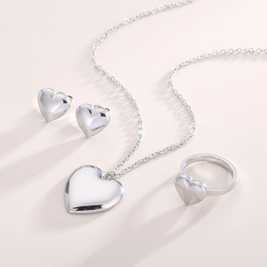 Flat lay of polished silver heart-shaped jewelry set including necklace, studs, and ring