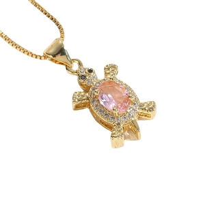 Collier tortue plaqué or 14K avec pierre rose et zircons sur fond blanc épuré et élégant