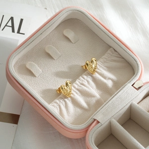 Detailed close-up of golden textured heart stud earrings inside a pink travel jewelry box